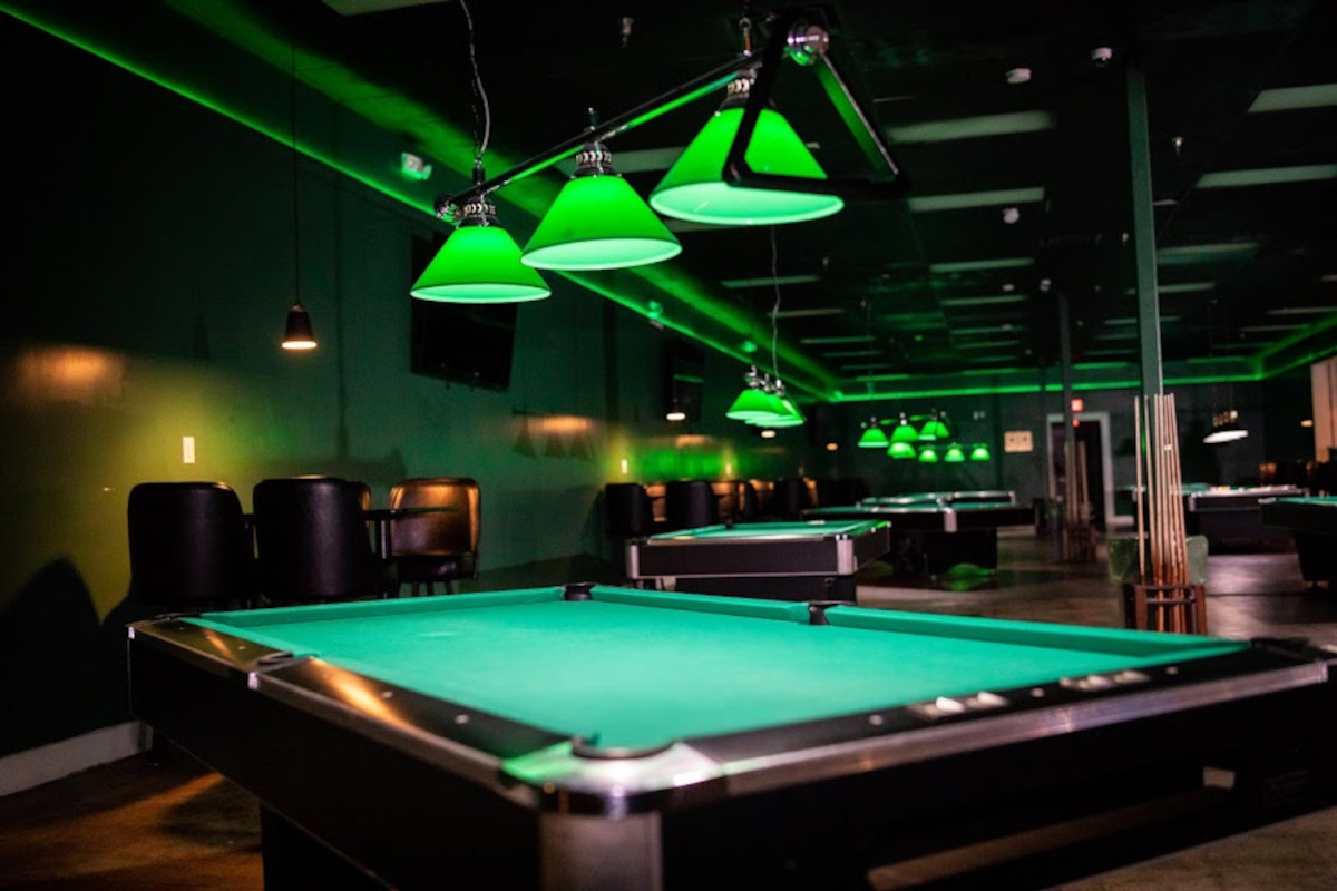 Pool tables under green lamps in the Ziggys game room